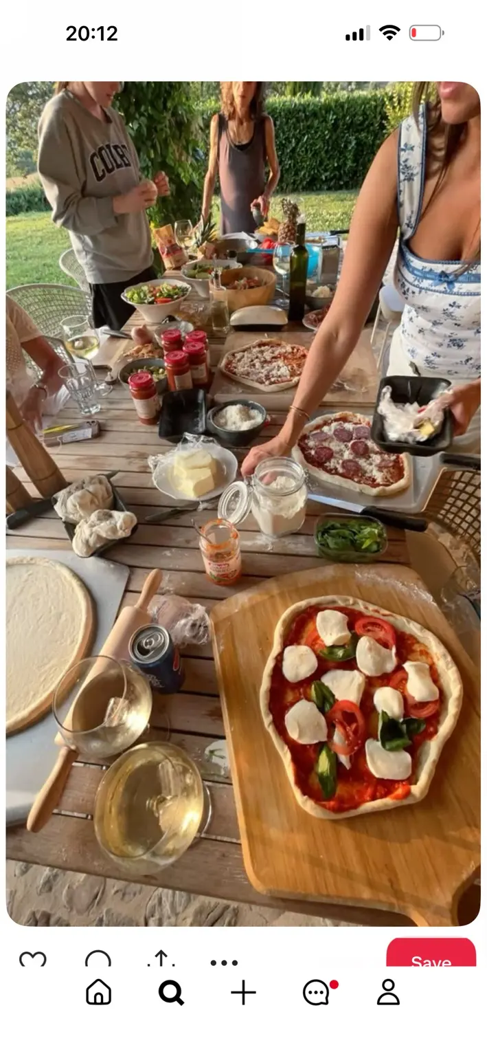 An outdoor table where friends prepare homemade pizzas