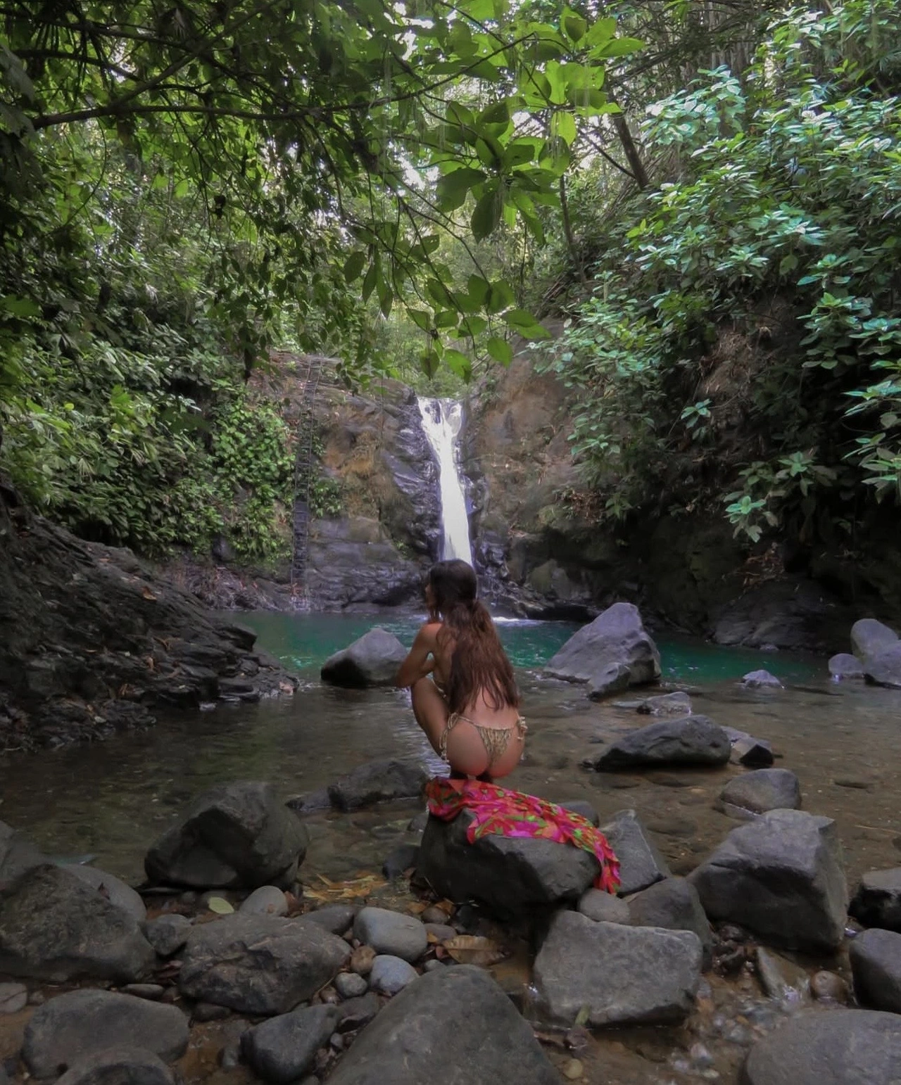 Kara sitting beside a waterfall surrounded by rainforest