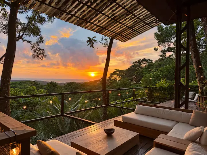 Covered terrace with cushioned seating overlooking the sea at sunset